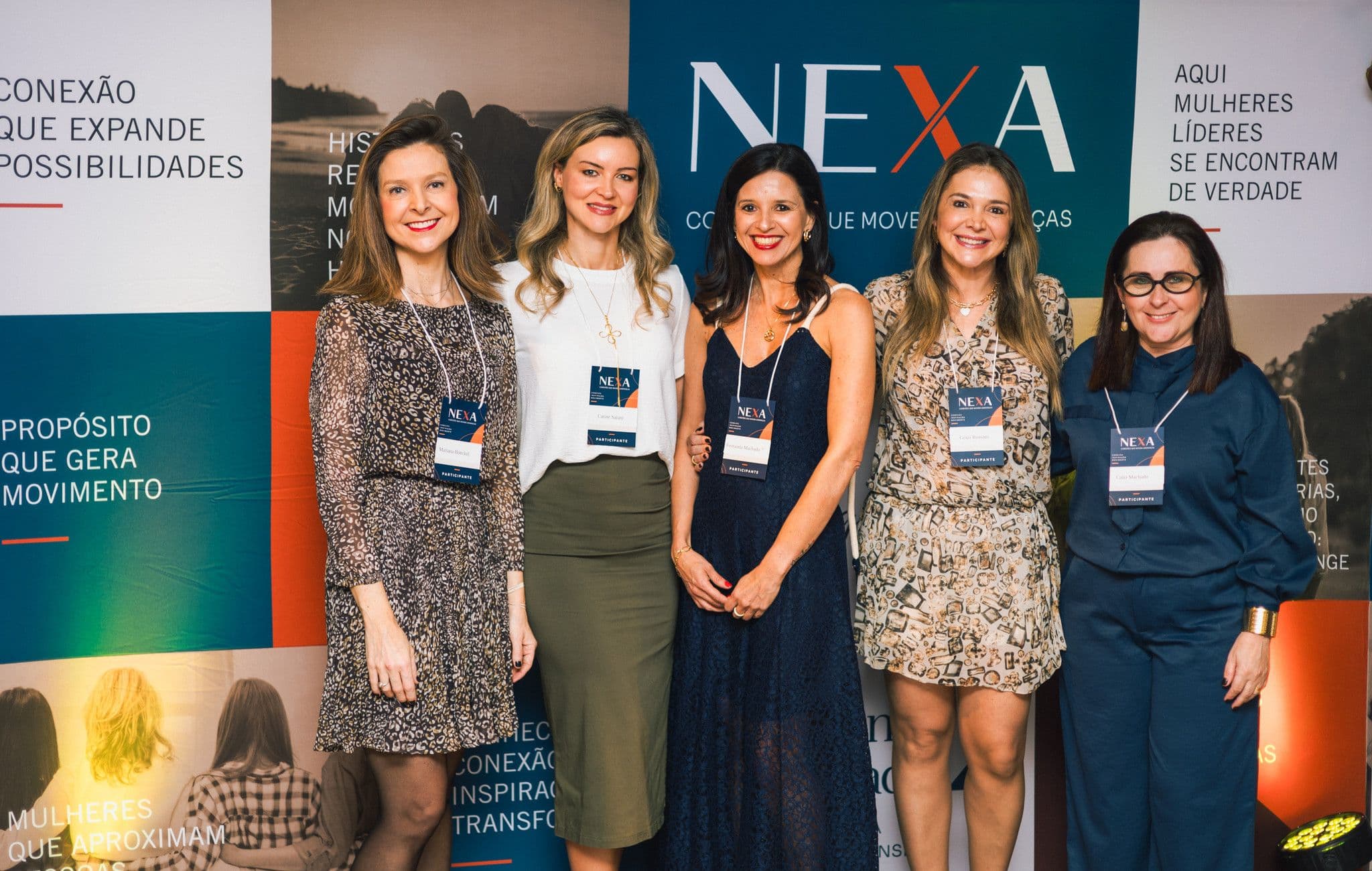 Fernanda Machado ao centro, com as convidadas do painel, posando diante do painel NEXA.