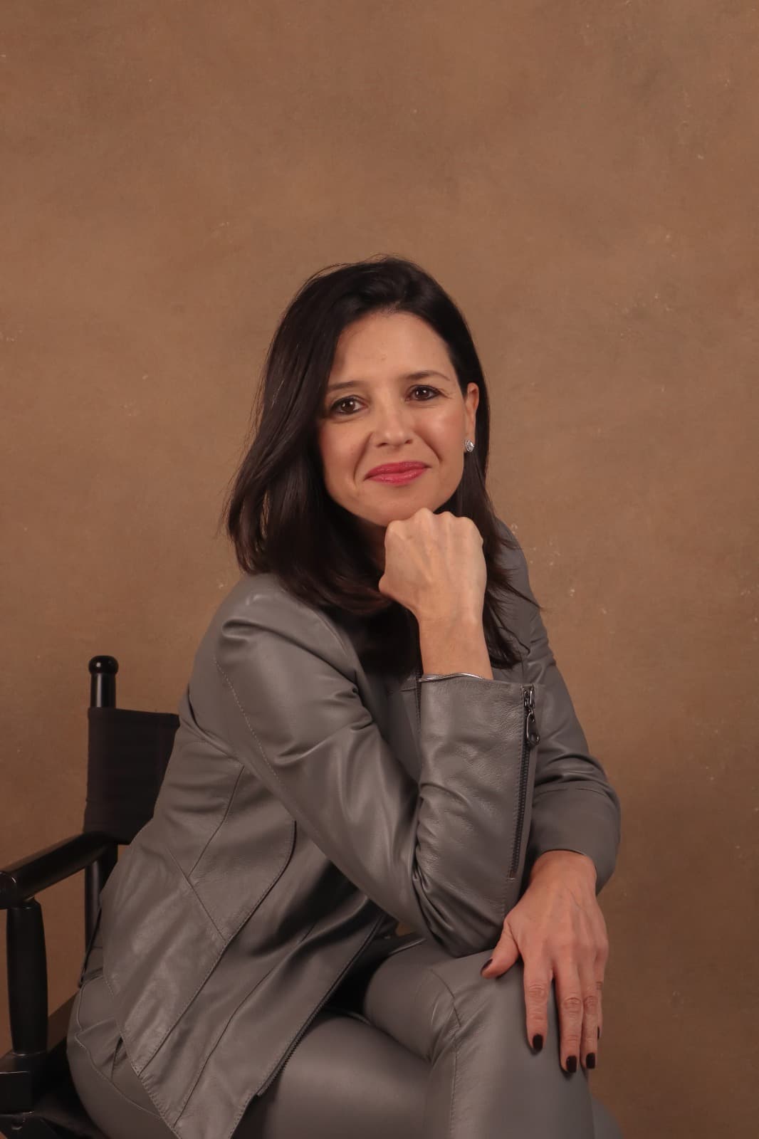 Fernanda Machado sentada, apoiando o queixo na mão, diante de parede de tom terroso.