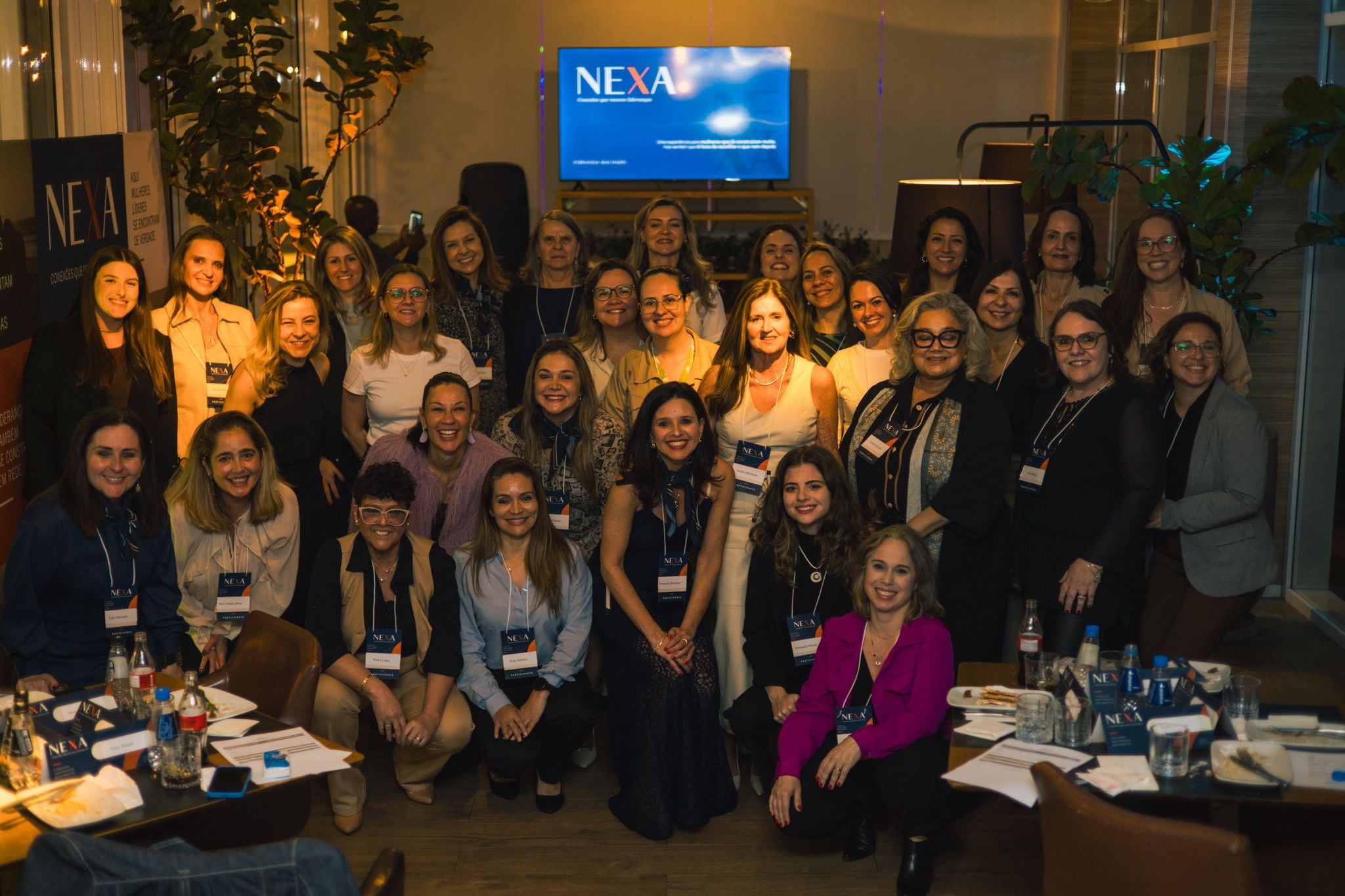 Foto de grupo com as participantes da noite reunidas diante da tela com a marca NEXA.